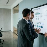 Geschäftsleute analysieren Compliance-Flussdiagramme für GDPR-konformen Web-Research auf einem großen Bildschirm in einem Konferenzraum.