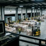 Drukke magazijnvloer met pallets naast een lege terminal door een vertraagde goedereningang WMS in het logistiek proces.