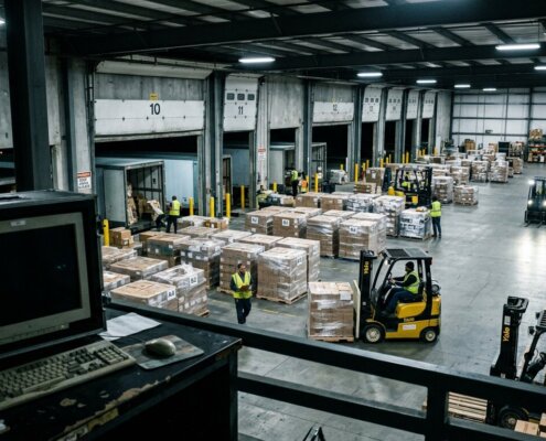 Drukke magazijnvloer met pallets naast een lege terminal door een vertraagde goedereningang WMS in het logistiek proces.
