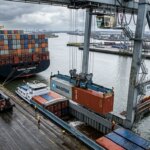 Kraan verplaatst containers van zeeschip naar binnenvaartschip voor emissiedata multimodaal transport onderzoek.