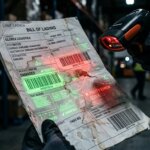Beschädigter Frachtbrief mit Daten-Overlays im Lager, was auf die Risiken von False Positives in der OCR-Logistik hinweist.