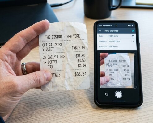 Eine Hand hält einen Beleg neben einer mobilen App für Spesenabrechnungen in einer modernen Büroumgebung – Best Practices der Verarbeitung.